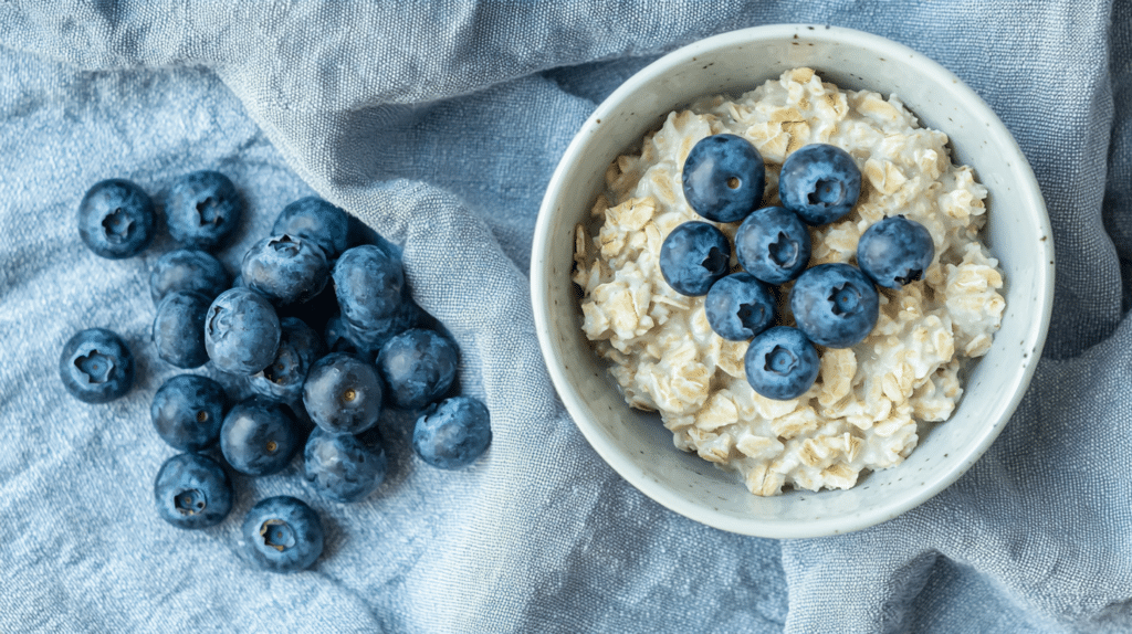 small white bowl of fresh blueberries beside a bowl of low FODMAP oatmeal on a linen cloth
