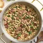 Chicken Sausage White Bean Skillet in a large skillet with a napkin and wooden spoon on the side