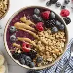 Overhead view of a smoothie bowl topped with granola, chia seeds, berries, and peanut butter
