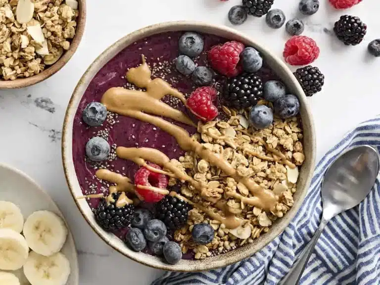 Overhead view of a smoothie bowl topped with granola, chia seeds, berries, and peanut butter