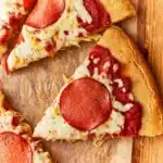 Sliced gluten-free pepperoni pizza on a wooden board with one slice pulled away