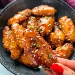 Hand holding a single crispy honey garlic chicken wing