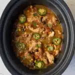 Cooked Santa Fe chicken in a black crockpot with sliced jalapeños and cilantro on top