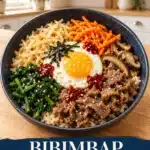 Korean bibimbap with rice, sliced beef, spinach, carrots, bean sprouts, mushrooms and a fried egg in a navy bowl