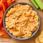 Creamy pimento cheese with shredded cheddar and red pimento pieces in a gray bowl, photographed directly overhead