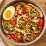 Chicken ramen with mushrooms, red pepper, scallions and an egg half in a gray bowl